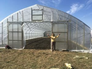 Laura Krouse standing by her newly finished high tunnel sent by Kate Edwards