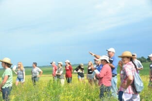 Standing on the high point of his farm, Aaron Lehman discusses small grains with attendees