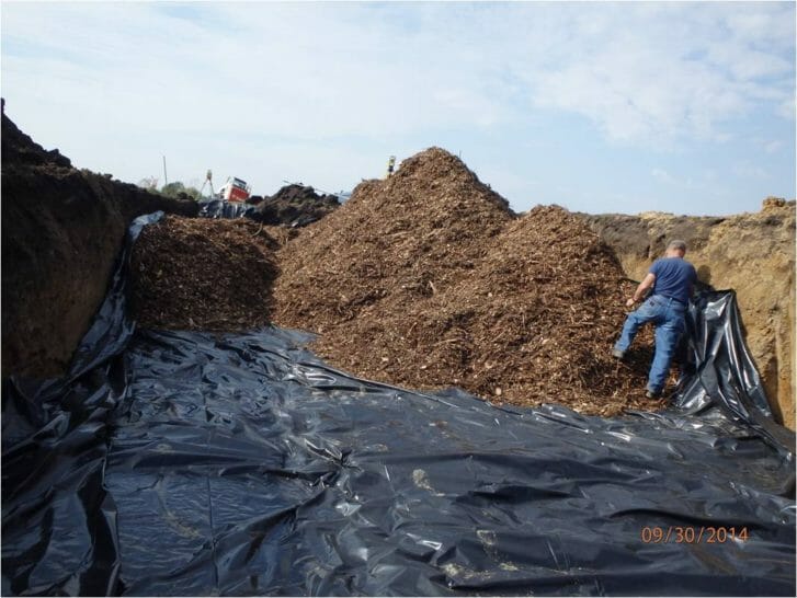 A large pile of wood chips are in a trench, as part of the process of constructing the bioreactor