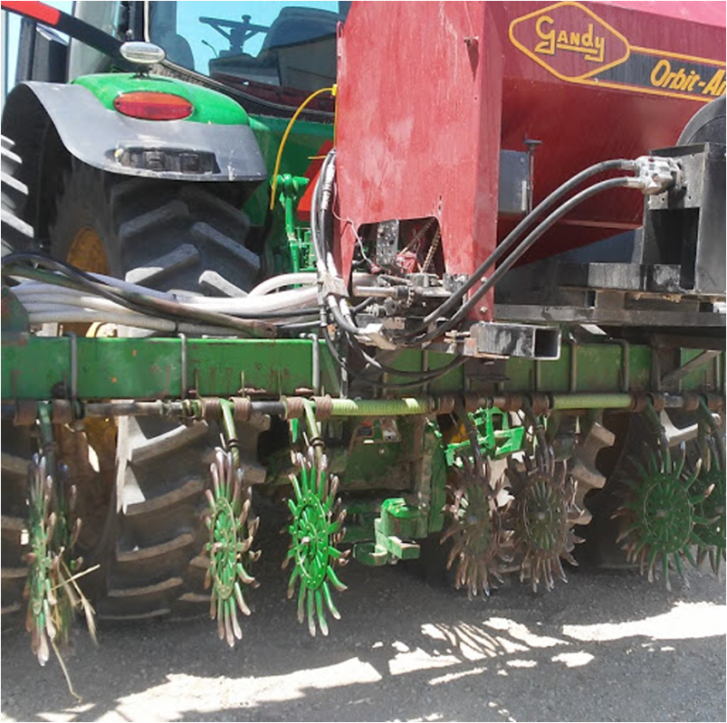 A green corn soybean planter sits in the frame with long fingered, sharp discs mounted on the back.