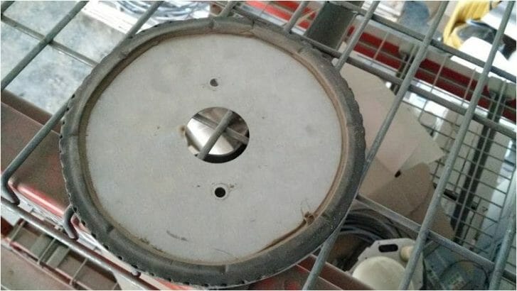 A round disc of metal sits on a crate with a large hole in the center. Around the rim a thin layer of shaped black foam rings it.
